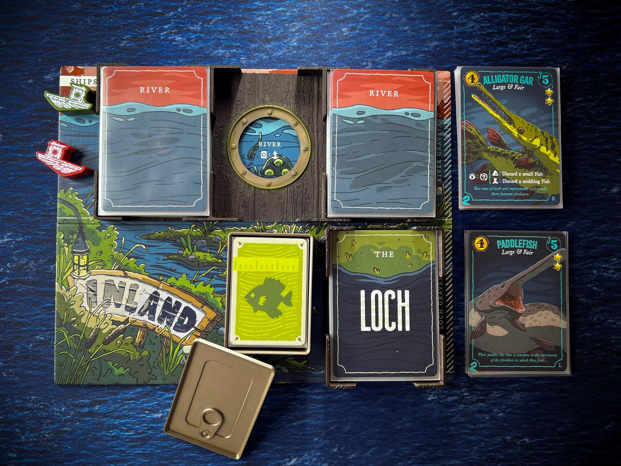 The Even Deeper Regrets expansion in play on a sea mat: a porthole wall between the River decks, the Loch tray and a sardine-tin card holder.