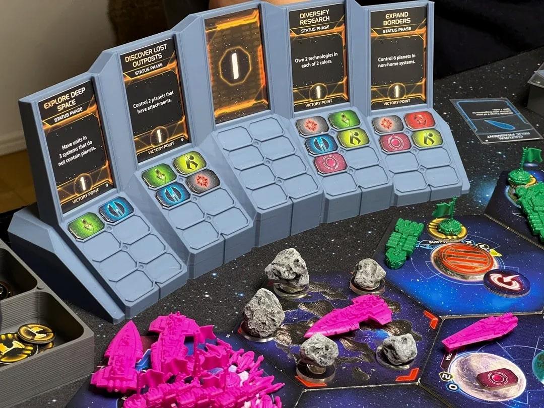 A printed Twilight Imperium public objectives display holding five cards and their control tokens, beside the galaxy map in play.