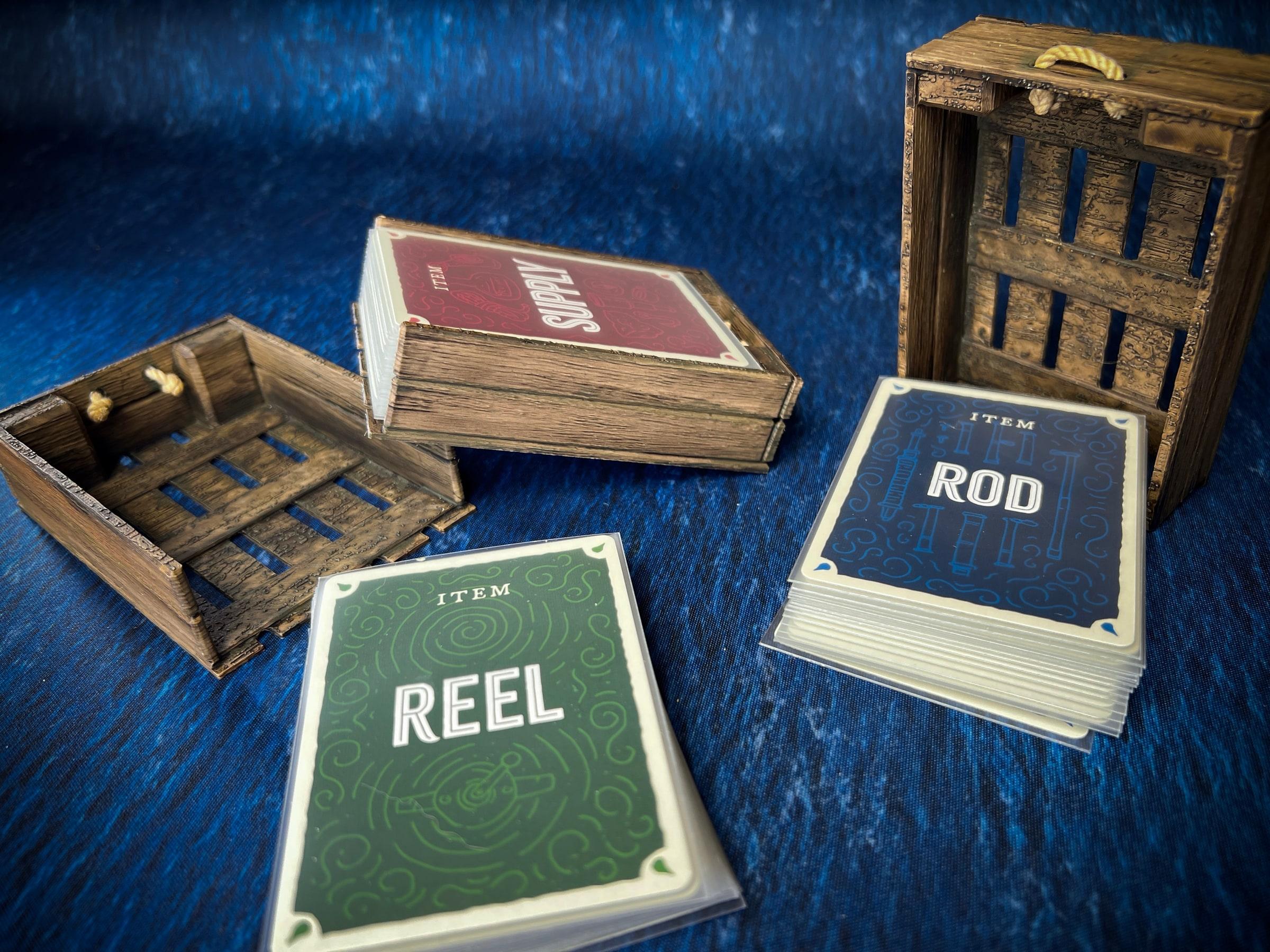 Printed wooden-look port crates from the Deep Regrets insert, stacked with the game's item cards on a blue sea mat.